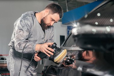 Araba tamircisi özel öğütücüyle araba cilalıyor ve araba tamirhanesindeki çiziklerden dolayı cila yapıyor. Profesyonel araba temizleme ve bakım konsepti