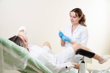 Jinekolog jinekoloji kürsüsünde oturan bir hastayı muayene ediyor.