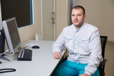 Tıbbi klinikte bilgisayar üzerinde çalışan erkek doktor.