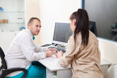 Genç bir erkek doktor hastane kliniğinde genç bir bayana muayene ve danışmanlık yapıyor. Profesyonel pratisyen hekim danışmanı teşhisi Tıbbi sağlık konsepti