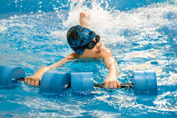 Junge schwimmt mit Wasserhanteln in der Hand im Schwimmbad — Stockfoto