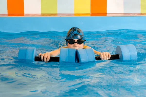 Chłopiec pływanie z hantlami wodnymi w rękach w basenie — Zdjęcie stockowe