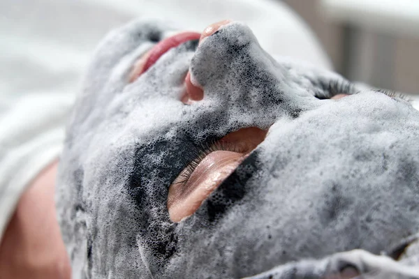 Ung kvinna med en svart syre bubbla mask på ansiktet i skönhetssalong — Stockfoto