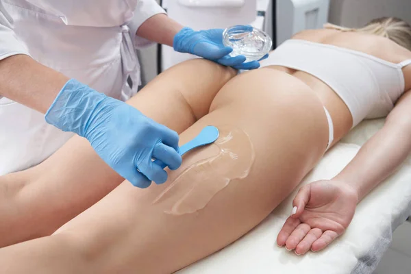 Cosmetólogo aplica un gel transparente a las piernas y las nalgas de los pacientes para el tratamiento de belleza — Foto de Stock