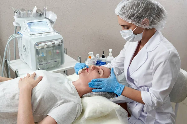 Jeune femme ayant un massage du visage en mousse. cosmétologue appliquer de la crème ou de la mousse sur le visage féminin pour nettoyer la peau — Photo