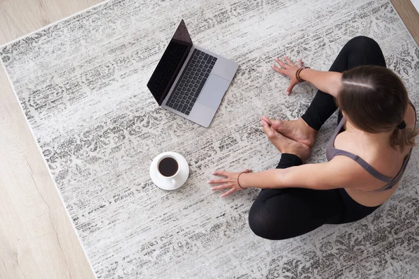 Sportovní mladá žena sedí na podlaze v obývacím pokoji cvičit jógu na online počítačové lekci. žena meditovat vlak doma sledování mají třídu na webcam na notebooku — Stock fotografie