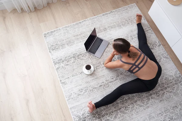 Спортивная молодая женщина сидит на полу в гостиной практикует йогу на онлайн компьютерном уроке. женщина медитировать поезд дома смотреть занятия на веб-камеру на ноутбуке — стоковое фото