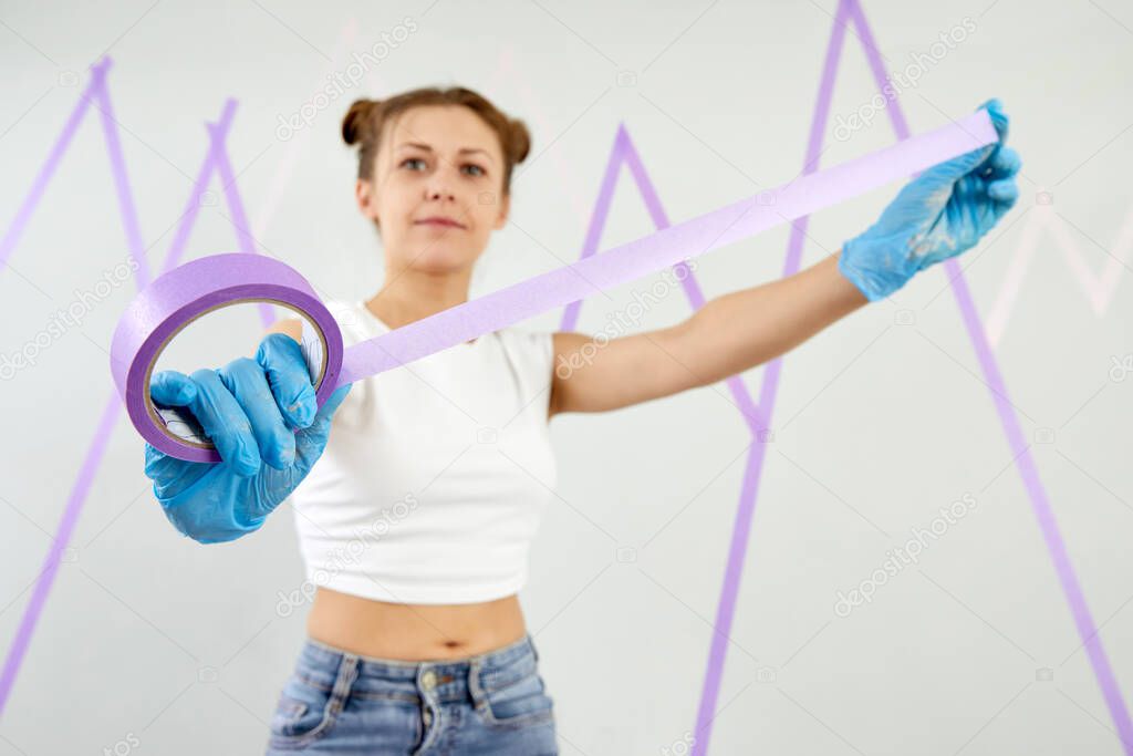 cheerful woman holding a masking tape working and redecorating in her new apartment. Decoration concept. Home made work painting a wall.