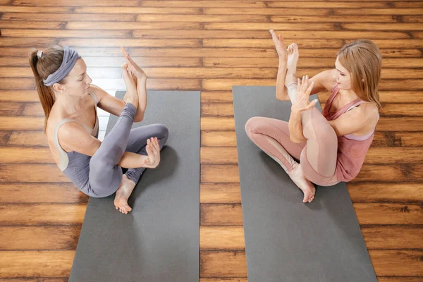 Twee volwassen vrouwen die zich uitstrekken op matten in yoga studio. Vriendschap en sport — Stockfoto