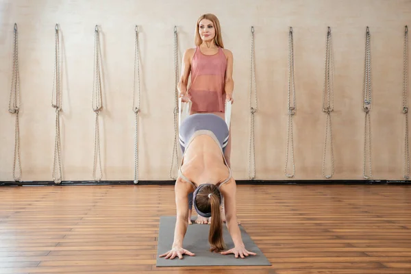 Couple of women doing stretching yoga exercises with the help of personal yoga teacher in yoga studio — Stock Photo, Image