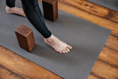 Yoga stüdyosunda yoga bloklarıyla bacaklarını esneten bir kadın görüntüsü.
