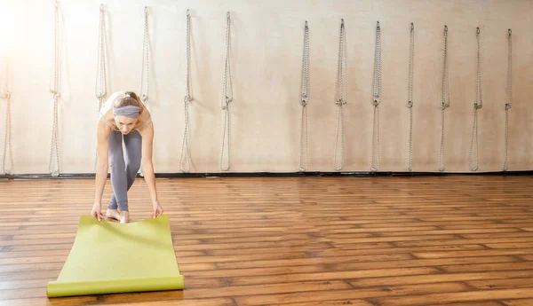 Ung kvinna som rullar yogamatta i yogastudion innan träningsklass. Kopiera utrymme — Stockfoto