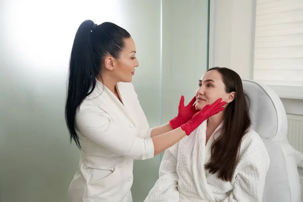 Kozmetológus vizsgálja a női arc ellenőrzése bőr állapotát a kozmetikai szalonban végzett bőrvizsgálat során — Stock Fotó