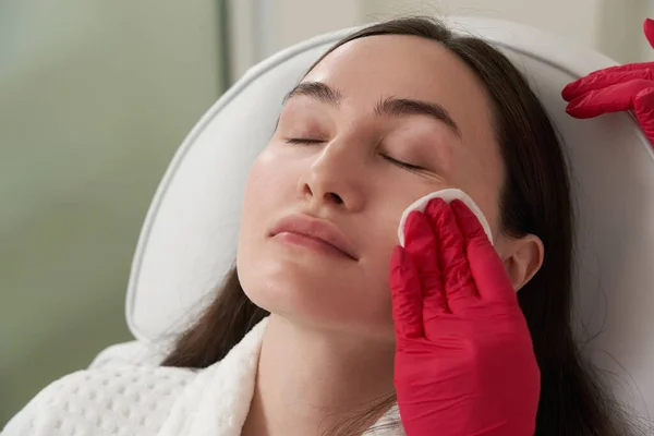 Cosmetólogo limpiando la cara de un paciente con almohadilla de algodón en salón de belleza y spa preparándose para el procedimiento — Foto de Stock