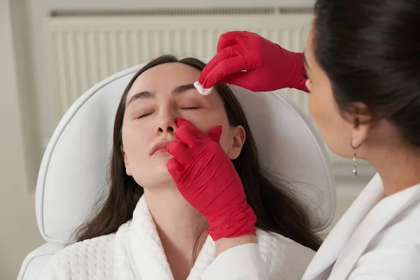 Cosmetólogo limpiando la cara de un paciente con almohadilla de algodón en salón de belleza y spa preparándose para el procedimiento — Foto de Stock