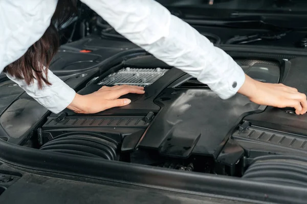 Egy fiatal nő áll az autó előtt nyitott motorháztetővel, aki a motorháztető alá néz. — Stock Fotó