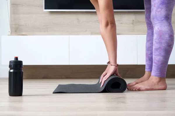 Bijgesneden beeld van vrouw vouwen zwarte yoga of fitness mat na het sporten thuis in de woonkamer. Gezond leven, yoga concepten — Stockfoto