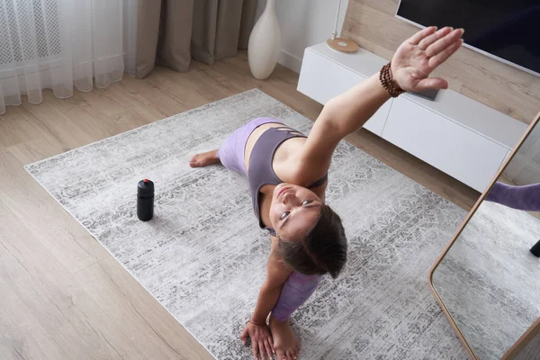 Jong sportief meisje dat thuis yoga beoefent in de woonkamer. Sport en fitness concept. Uitzicht van bovenaf — Stockfoto