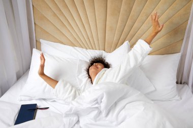 Gülümseyen kadın yatakta uyanıyor ve kollarını kaldırıyor.