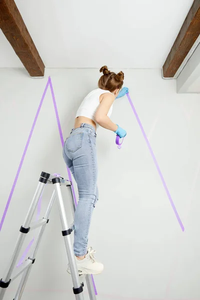 Mujer joven preparando la pared para pintar de pie en la escalera aplicando cinta adhesiva en la pared. Proyecto Diy — Foto de Stock