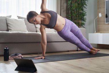 Fit Kadın tabletindeki online eğitim programını kullanarak minderinde yoga yapıyor.