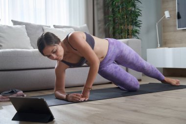Fit Kadın tabletindeki online eğitim programını kullanarak minderinde yoga yapıyor.