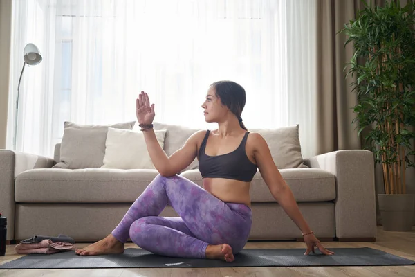Vrouw doen yoga stretching oefening zitten op mat in de buurt bank in woonkamer thuis — Stockfoto