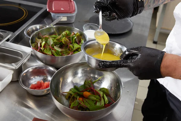 Closeup of chef hands preparing salad pouring sauce in a restaurant kitchen — Stock Photo, Image