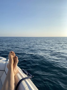 Kadın ayaklarını teknenin kenarına dayayıp dinleniyor. Seyahat kavramı.