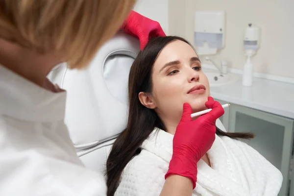 女性美容师在女性脸上画一条白线，为手术做准备。面部护理概念 — 图库照片