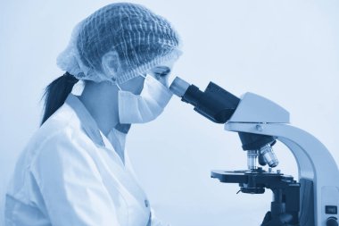 Modern kimya laboratuvarında mikroskopla araştırma yapan kadın bilim adamı. Mikroskop kullanarak kan örneklerini analiz ediyorum. Mavi tonlama