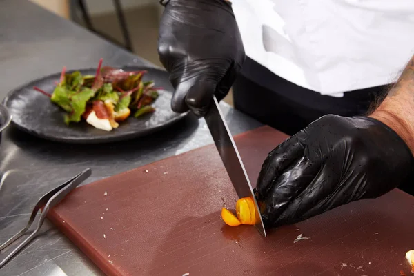 Fechar as mãos do chef cortando tomaos preparando salada em uma cozinha de restaurante — Fotografia de Stock