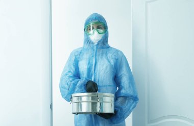 Autoclave Sterilizatör kutusunu tutan kişi koruyucu üniforma giyiyor. mavi tonlu