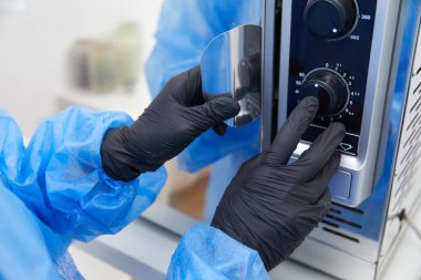 Modern laboratuvar otoklav sterilizatörünü çalıştıran bir laboratuvar çalışanı.