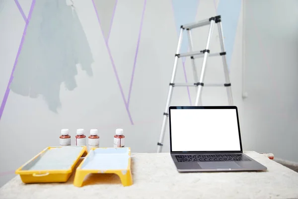笔记本电脑立在桌子上，白色的复制空间与墙壁在背景图片上的模型。梯子和油漆。翻新和家庭装修概念 — 图库照片