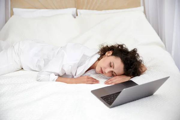 Beyaz yatakta dizüstü bilgisayar kullandıktan sonra uyuyan kıvırcık kız internette arkadaşlarıyla sohbet ediyor. — Stok fotoğraf