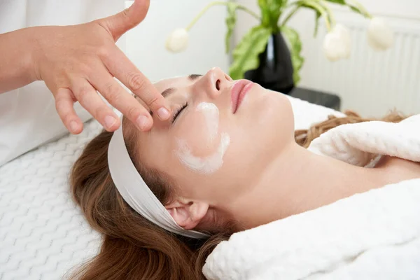 Cosmetologue appliquer de la crème sur le visage féminin. Femme ayant un traitement du visage dans le salon de spa — Photo