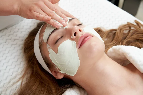 美容院的美容师在女性脸上涂上年轻的面罩。面部治疗概念 — 图库照片