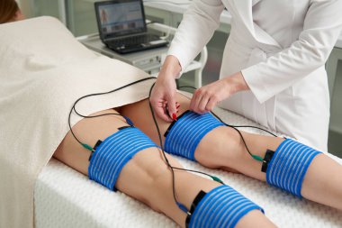 Güzellik salonundaki bir kadının bacaklarındaki miostimülasyon prosedürü. Vücuda elektrostimülasyonla bakmak, aşırı ağırlığı azaltmak.