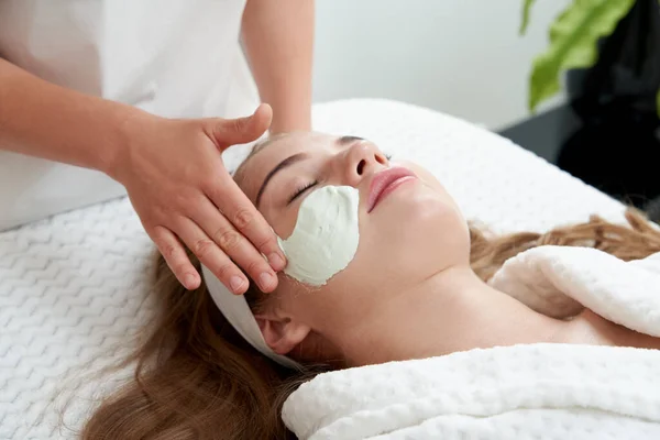 Cosmetologist applying rejuvenating facial mask on a female face in beauty salon. Facial treatment concept — Stock Photo, Image