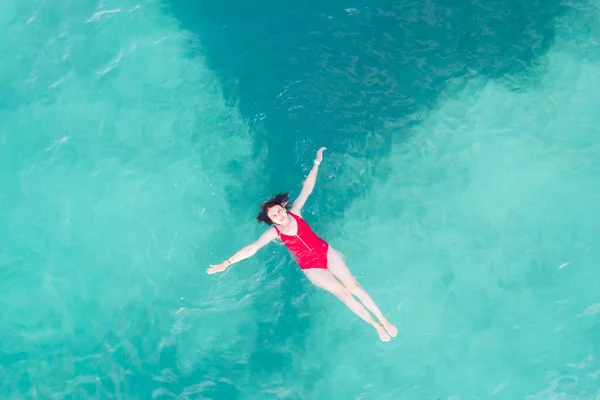 Luftaufnahme einer Frau in rotem Badeanzug, die auf einer transparenten türkisfarbenen Wasseroberfläche am karibischen Strand liegt. Reise- und Urlaubskonzept. Tropischer Hintergrund mit Kopierraum — Stockfoto