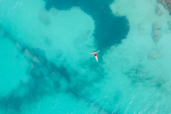 Luftaufnahme einer Frau in rotem Badeanzug, die auf einer transparenten türkisfarbenen Wasseroberfläche am karibischen Strand liegt. Reise- und Urlaubskonzept. Tropischer Hintergrund mit Kopierraum — Stockfoto