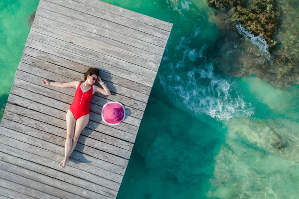 Vista superior de la mujer acostada en el muelle de madera en el soleado día de verano en Cancún, México. Mujer sexy joven en el traje de baño rojo en el Caribe. Verano playa vacaciones concepto —  Fotos de Stock
