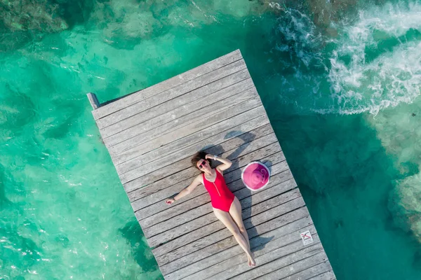 Luchtfoto van vrouw liggend op houten pier op zonnige zomerdag in Cancun, Mexico, bovenaanzicht. Jonge sexy vrouw in het rode badpak in de zomer in Caribbean. Zomer strand vakantie concept — Stockfoto