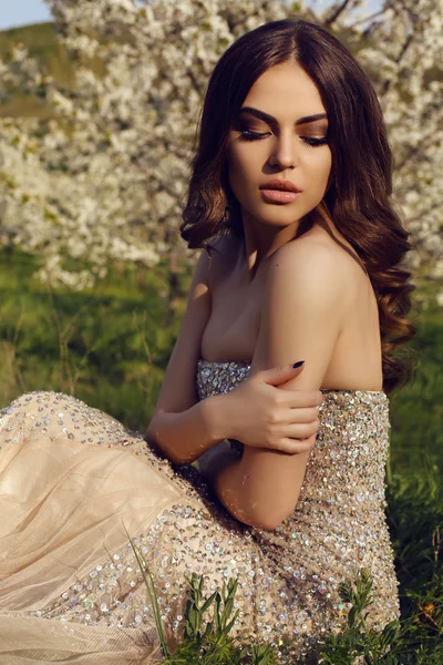 Gorgeous sensual woman with dark hair in elegant dress posing in blossom garden — Stockfoto