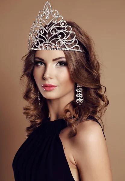 Beautiful glamour girl with dark curly hair with precious crown on head — Stock Fotó