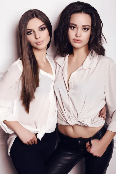 Две красивые молодые женщины с темными волосами и вечерним макияжем, одетые в элегантную одежду — стоковое фото