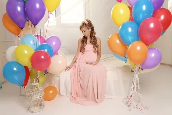Zwangere vrouw met lang blond haar in elegante jurk, met een heleboel kleurrijke lucht ballonnen — Stockfoto