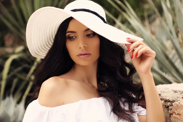 Wunderschöne Frau mit dunklen Haaren in elegantem weißen Kleid und Hut — Stockfoto