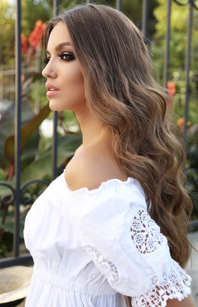 Schöne Frau mit dunklem lockigem Haar und hellem Make-up in elegantem Kleid — Stockfoto
